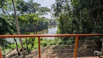 A view from a wooden balcony with a metal railing overlooking a river surrounded by dense forest.