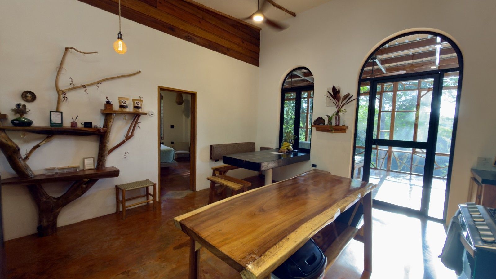 A spacious room with a large wooden table, a ceiling fan, and a view through a large arched window.