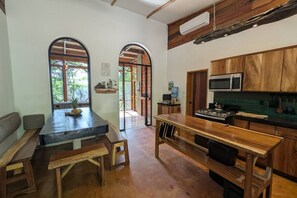 A kitchen with wooden cabinets, a stove, and a microwave. There is a dining area with a bench and a table.