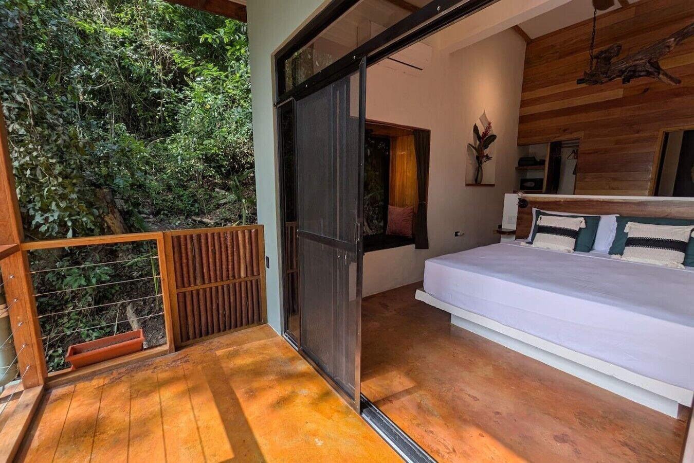 A bedroom with a bed, a wooden floor, a sliding door, and a view of greenery outside.