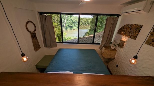 A room with a bed, a window with a view of a lake, and two wall-mounted light fixtures.