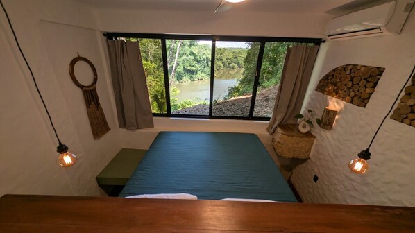 A room with a bed, a window with a view of a lake, and two wall-mounted light fixtures.