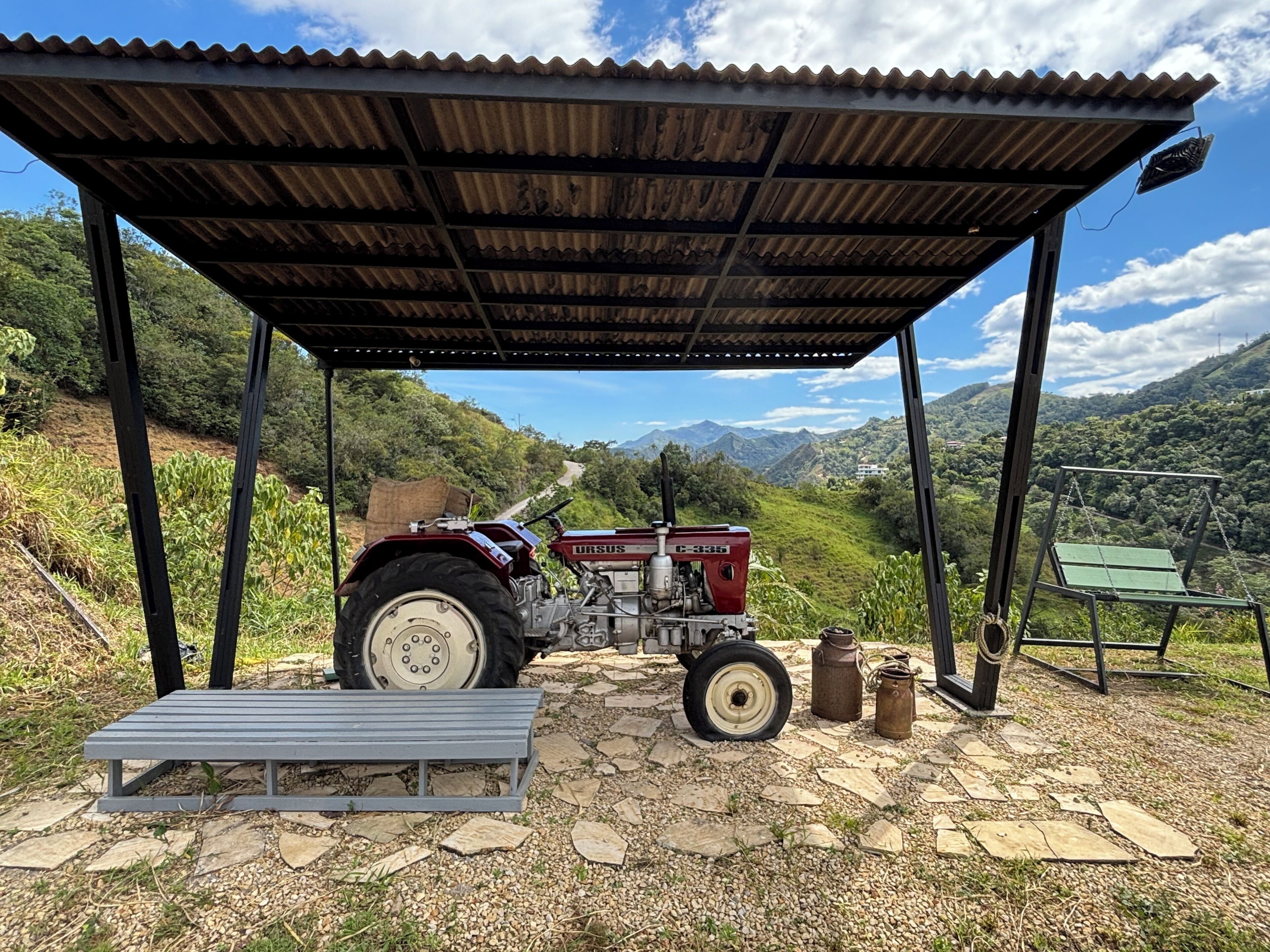 A red tractor parked under a metal shelter with a view of a mountainous landscape.