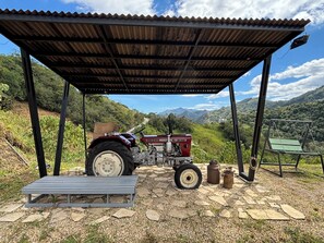 A red tractor parked under a metal shelter with a view of a mountainous landscape.