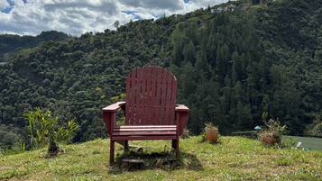 Una silla Adirondack roja sobre una colina cubierta de hierba con una montaña boscosa al fondo.