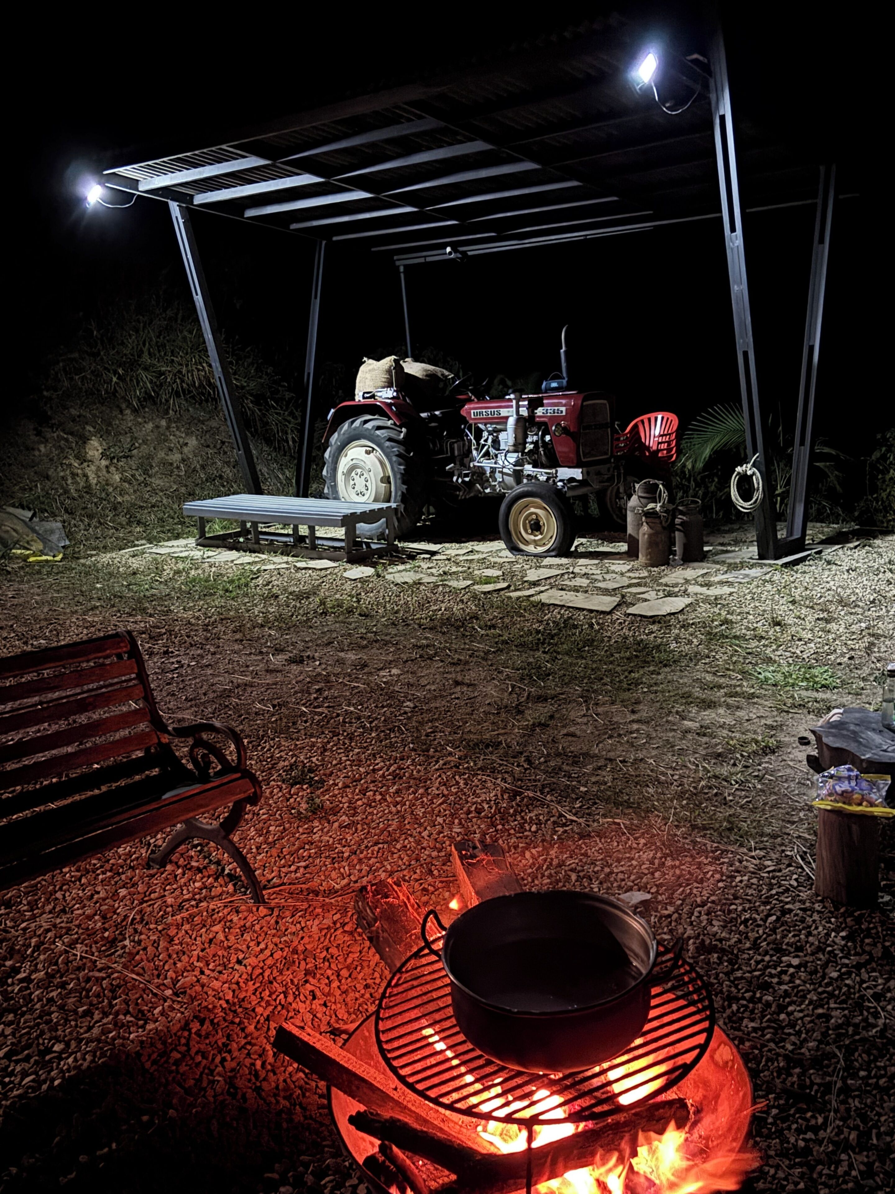 A covered outdoor area with a tractor, a bench, and a campfire.