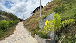 A pathway leading to a building with a yellow logo, surrounded by greenery and a hilly landscape. - Magma Ecohotel—Onix Cabin (La Vega)