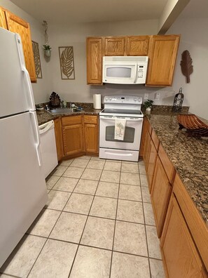 A kitchen with wooden cabinets, a white refrigerator, a microwave, and a stove. - Cozy 1-bedroom condo in peaceful Biloxi with AC and gym access for 2 adults only (Biloxi)
