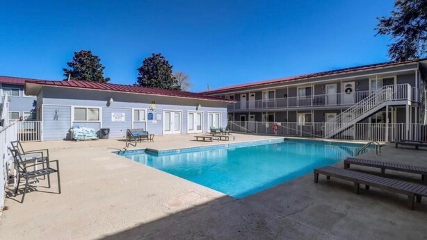 Un motel con piscina, asientos al aire libre y una zona techada.