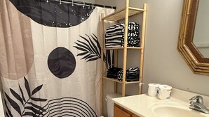 Un baño con inodoro, lavamanos, espejo y repisa con toallas dobladas.