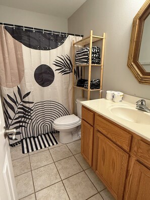 A bathroom with a toilet, a sink, a mirror, and a shelf with folded towels. - Cozy 1-bedroom condo in peaceful Biloxi with AC and gym access for 2 adults only (Biloxi)