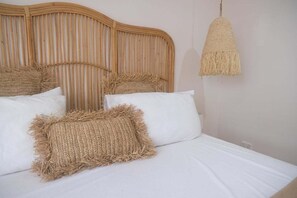 Ein Bett mit einem gewobenen Kopfteil, weißer Bettwäsche und einer hängenden Leuchte.