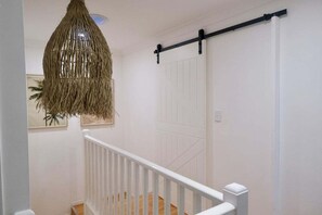 Eine Treppe mit weißer Geländer, eine hängende gewebte Leuchte und eine Schiebetür im Scheunenstil.