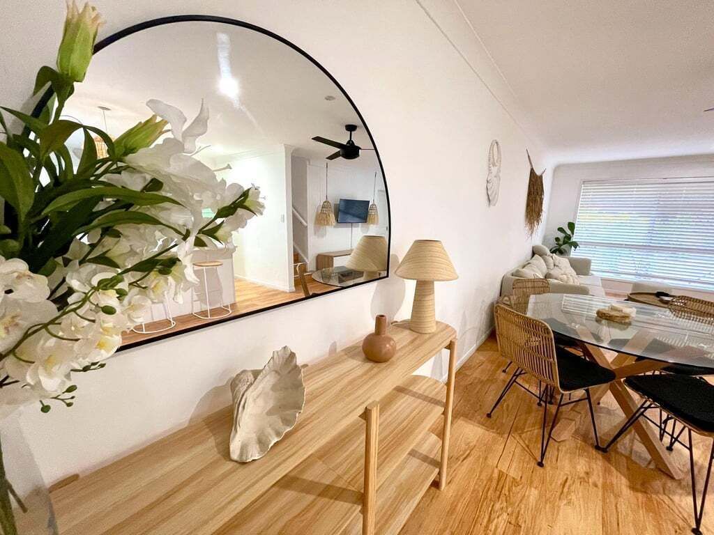 A modern interior with a round table, chairs, a mirror, a lamp, and a decorative plant.