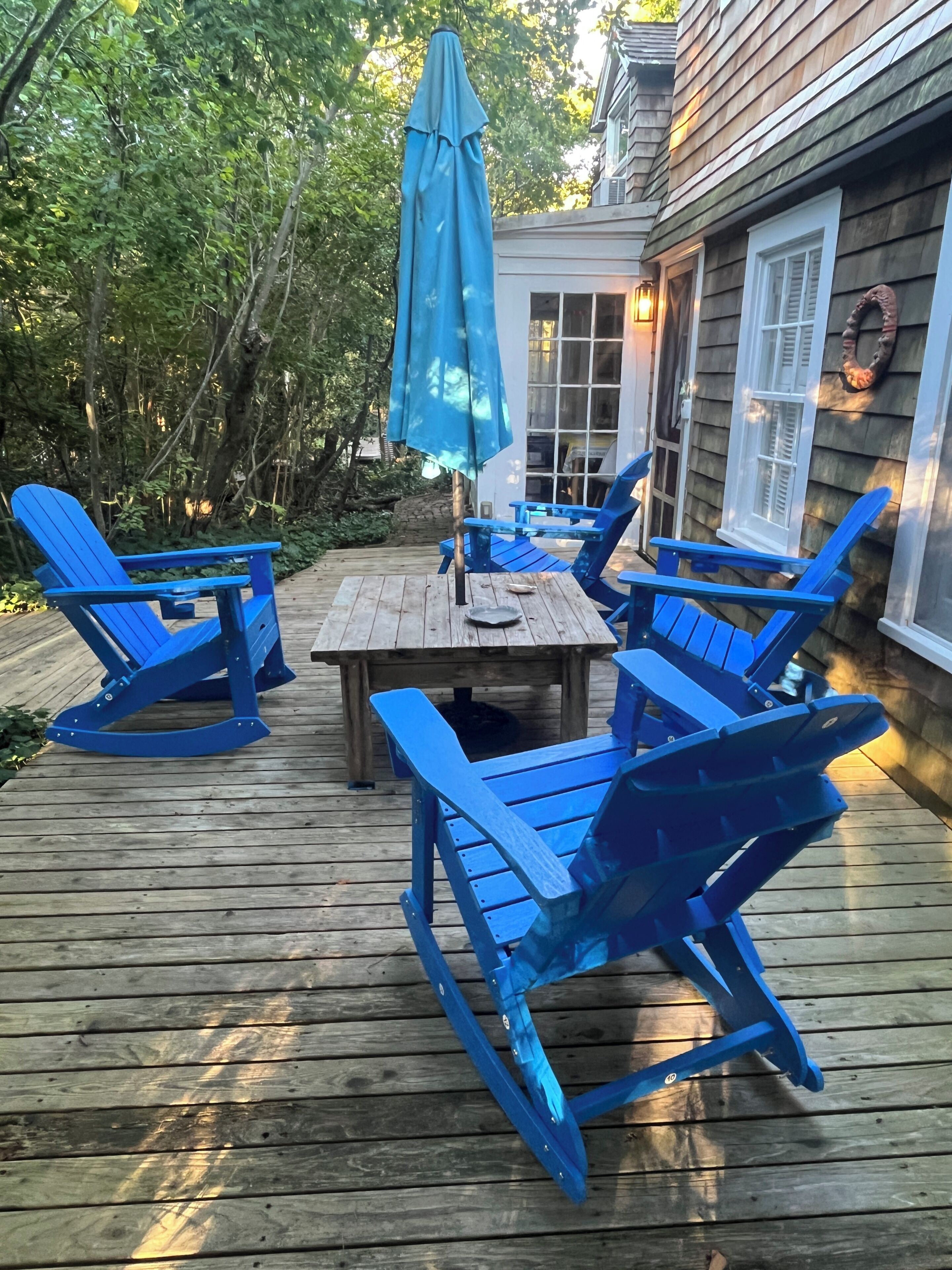 Une terrasse en bois avec une table et des chaises bleues, entourée de verdure.
