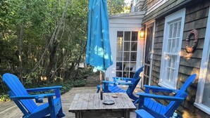 A wooden deck with a table and blue chairs, surrounded by greenery.