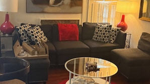 A living room with a sofa, a glass coffee table, and a red rug.