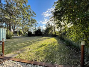 A grassy backyard with a wooden deck, a metal fence, and trees. - River to the Sea - Jervis Bay (Myola)