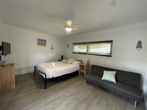 A bedroom with a bed, a sofa, a ceiling fan, a window with blinds, and a wall-mounted TV. - River to the Sea - Jervis Bay (Myola)
