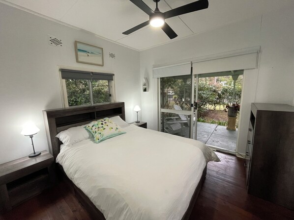 A bedroom with a bed, a ceiling fan, a window, and a door leading to an outdoor area. - River to the Sea - Jervis Bay (Myola)