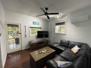 A living room with a leather sofa, a wooden coffee table, a television, and a ceiling fan. - River to the Sea - Jervis Bay (Myola)