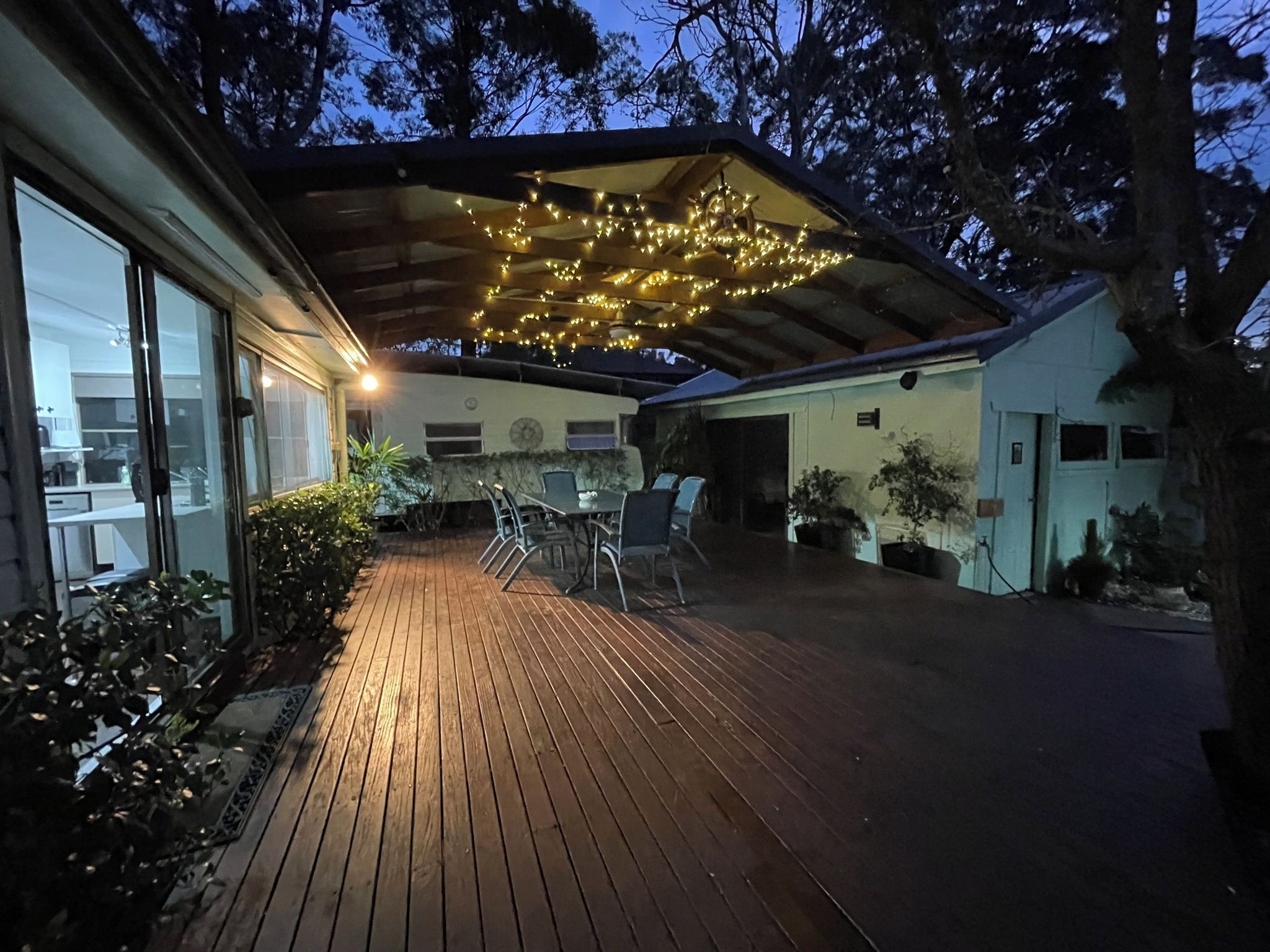 Un patio al aire libre techado con cubierta de madera, zona de estar y luces colgantes.