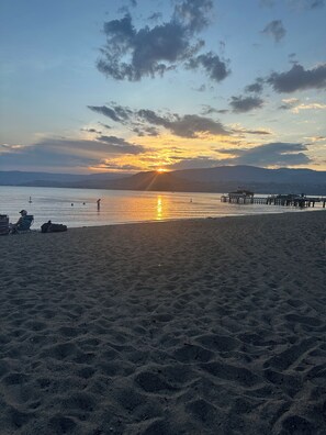 Een strand met een zonsondergang, rustig water en een steiger.