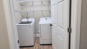 A laundry room with two washing machines, a ceiling light, and a metal shelving unit. - 3-bedroom house in fabulous Winston-Salem with cool AC breeze (Winston-Salem)