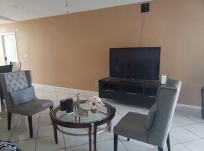 Ein Wohnzimmer mit Fernseher, zwei Sesseln, einem Couchtisch mit Dekoration und einer schwarzen Unterhaltungsanlage.