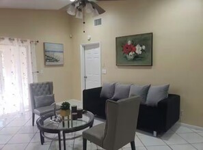A living room with a round glass table, two armchairs, a sofa, a ceiling fan, and two paintings on the walls. - Lakefront Oasis: Spacious 3BR/2BA West Palm Beach House (West Palm Beach)