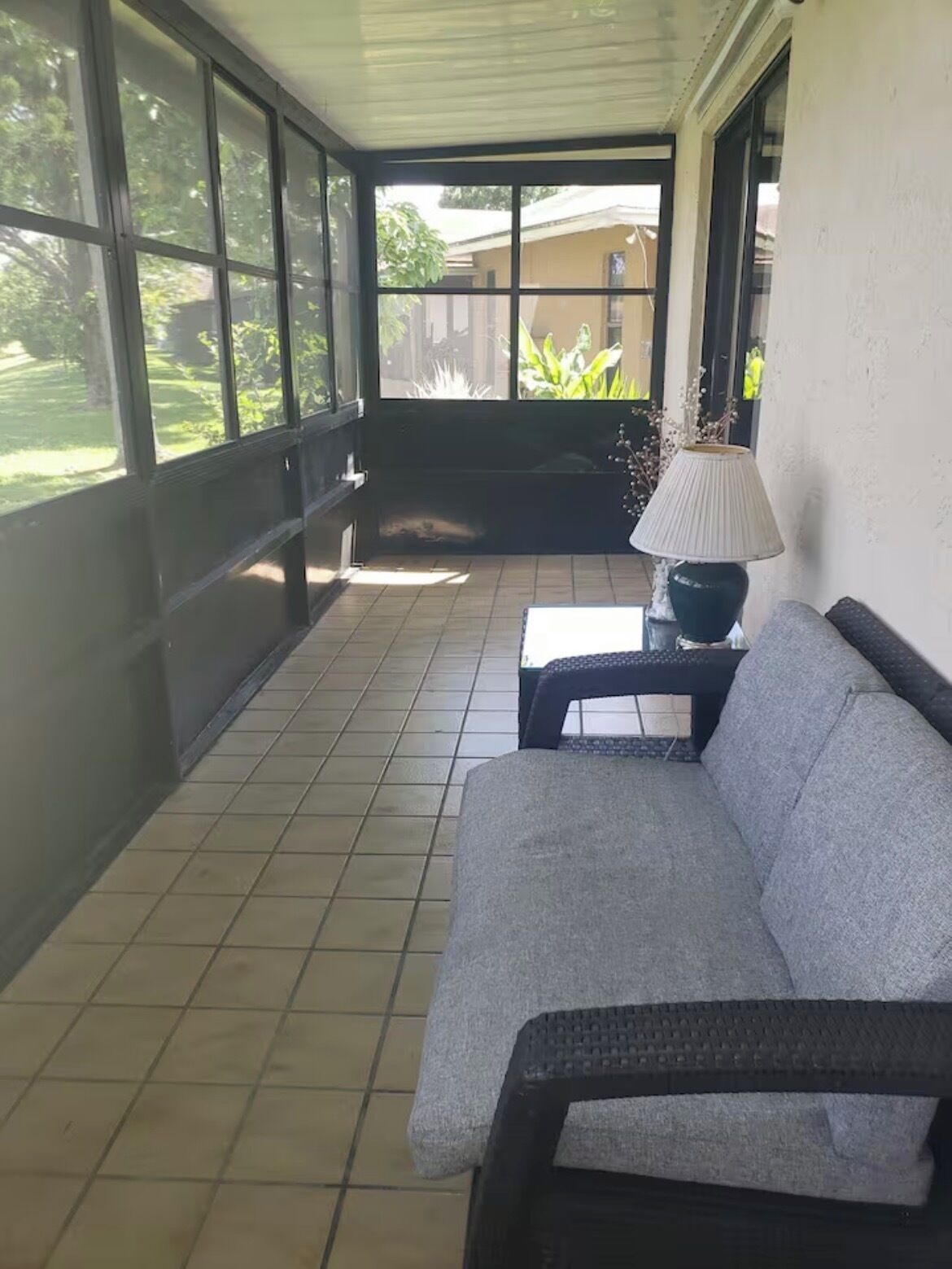 A covered patio area with a sofa, a table, and a lamp.