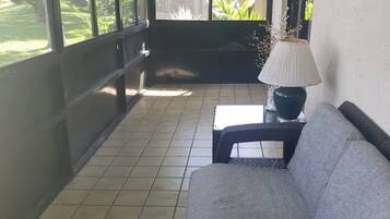 A covered patio area with a sofa, a table, and a lamp.