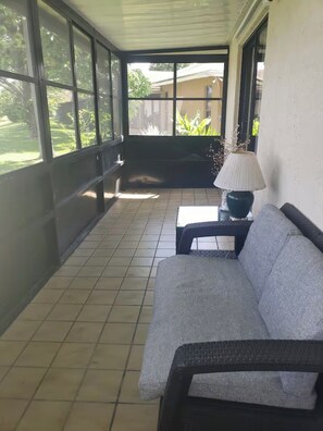 A covered patio area with a sofa, a table, and a lamp. - Lakefront Oasis: Spacious 3BR/2BA West Palm Beach House (West Palm Beach)