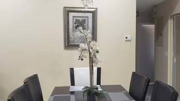 A dining area with a rectangular table, six chairs, a chandelier, a framed picture, and a potted plant.