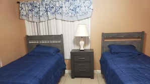 Une chambre avec deux lits simples, une table de chevet avec une lampe et une fenêtre avec des rideaux.