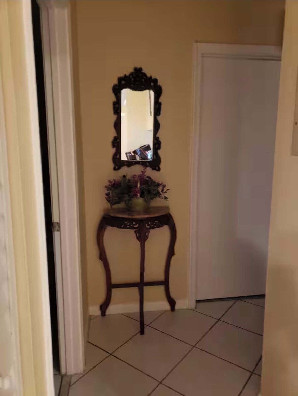 Un couloir avec une porte, un miroir et une petite table sur laquelle est posé un vase de fleurs.