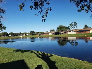 A tranquil outdoor area with a pond, grass, and buildings in the background. - Lakefront Oasis: Spacious 3BR/2BA West Palm Beach House (West Palm Beach)