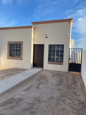 A two-story building with a flat roof, a front door, and two windows with metal bars. - VAROVI Cottage (Puerto Peñasco)