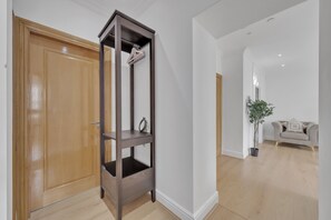 A hallway with a wooden door, a dark wooden shelf unit, a potted plant, and a light-colored sofa. - Charming 3B Apartment in Paddington Station (London)