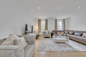 A modern living room with a sofa, armchair, coffee table, and TV. - Charming 3B Apartment in Paddington Station (London)