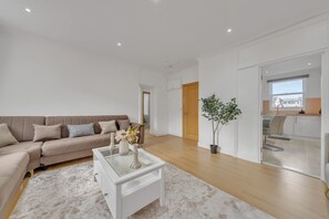 A modern living room with a beige sofa, a glass coffee table, and a potted plant. - Charming 3B Apartment in Paddington Station (London)