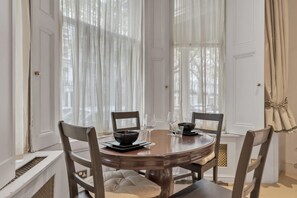 Ein Esszimmer mit einem runden Tisch, vier Stühlen und einem Fenster mit durchsichtigen Vorhängen.