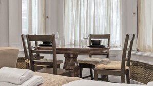 A dining area with a round table, four chairs, and a window with sheer curtains. - Modern Studio in Knightsbridge Greater London (London)