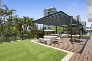Una terrazza esterna con zona salotto coperta, un prato e vista sugli edifici circostanti.