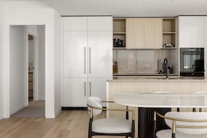 Eine moderne Küche mit weißen Schränken, einer zentralen Kochinsel mit Sitzgelegenheiten und einem schwarzen Kühlschrank.