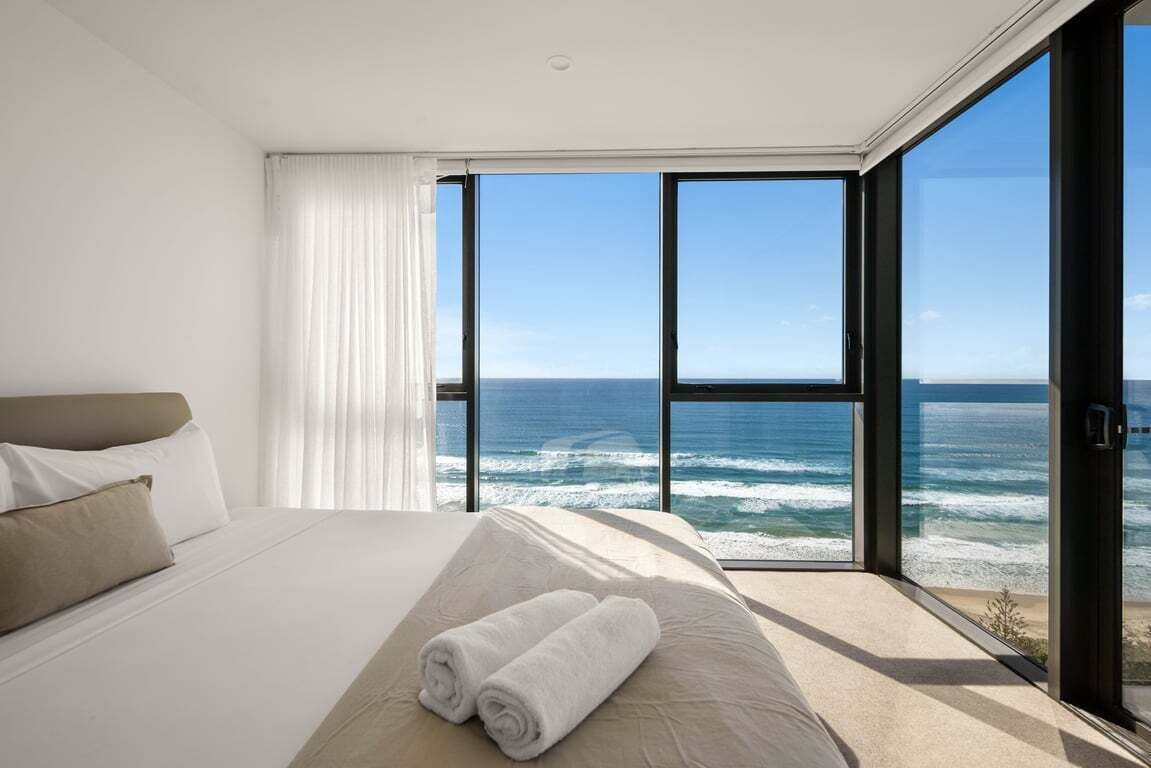 Une chambre d’hôtel moderne avec un grand lit, une vue sur l’océan et une porte-fenêtre coulissante.