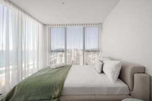 Ein Schlafzimmer mit einem Bett, Blick auf die Stadt und transparenten Vorhängen.