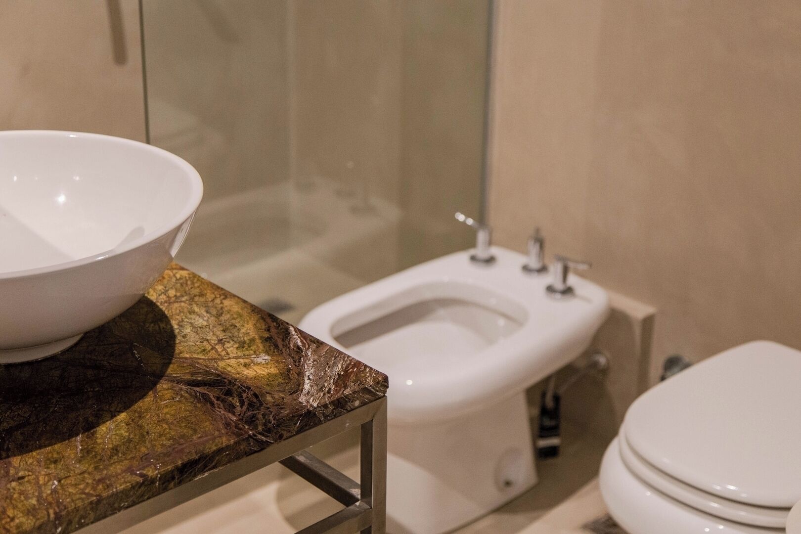 A bathroom with a marble countertop, a white sink, a toilet, and a glass shower enclosure.