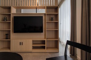 A modern living room with a large flat-screen TV, wooden shelving, and a dining area. - Recoleta Prime Location | New Studio - Coworking - BBQ (Buenos Aires)