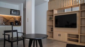 Un espai modern d'estar amb zona de cuina, taula de menjador i un gran televisor de pantalla plana muntat sobre una paret de fusta.